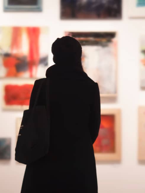 Silhouette of back of woman with hat bag looking at gallery wall with colourful art