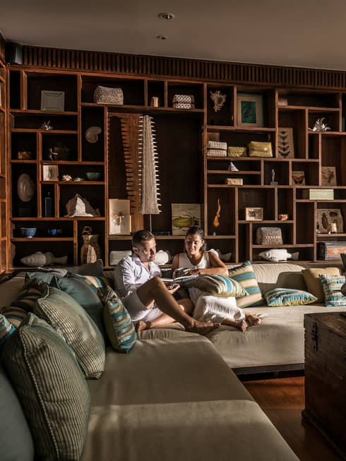 Couple relaxes on oversized plush L-shaped sofa by open door with flowing curtains