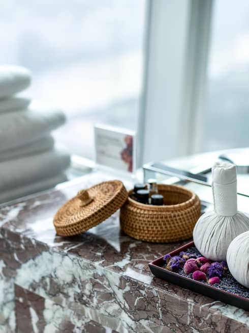 Luxury bath amenities sit atop a marble countertop beside a bathtub by a large window