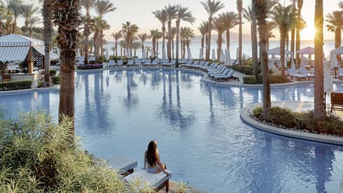 Person sits on side of luxury hotel pool surrounded by palm trees