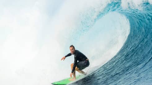 Surfer rides surfboard on large wave, two surfers swimming in water