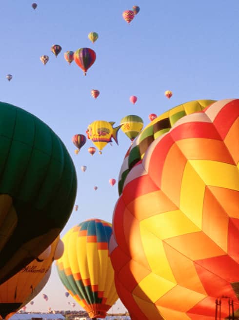 Clusters of colourful hot air balloons rising into blue sky