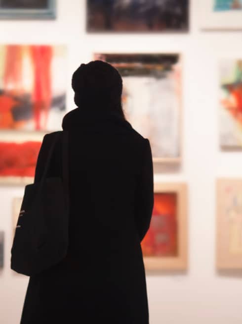 Silhouette of back of woman with hat bag looking at gallery wall with colourful art