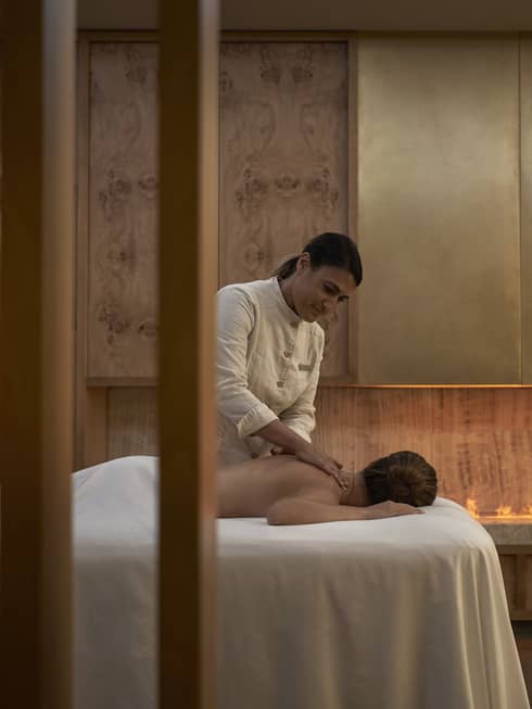 Person facedown on white spa table receiving massage from spa therapist