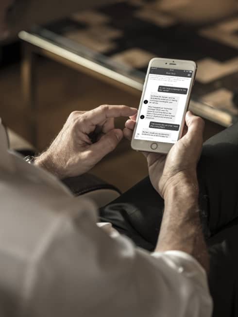 Man wearing suit looks down at text messages from spa on smart phone in lounge