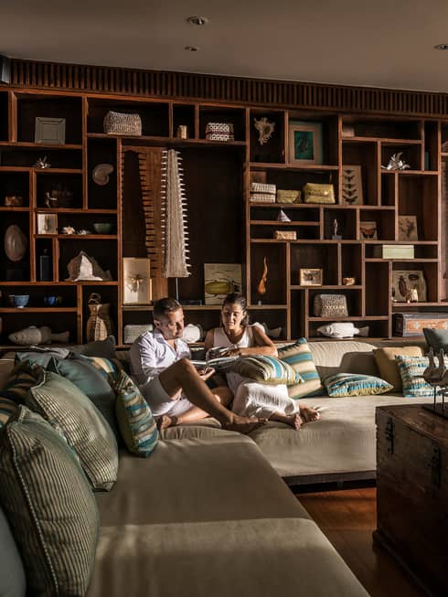 Couple relaxes on oversized plush L-shaped sofa by open door with flowing curtains
