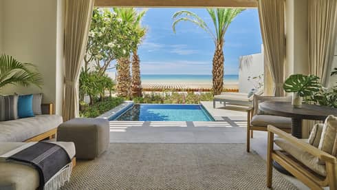Luxurious ocean-view casita room with a plunge pool, surrounded by greenery and palm trees and featuring comfortable indoor seating and a table
