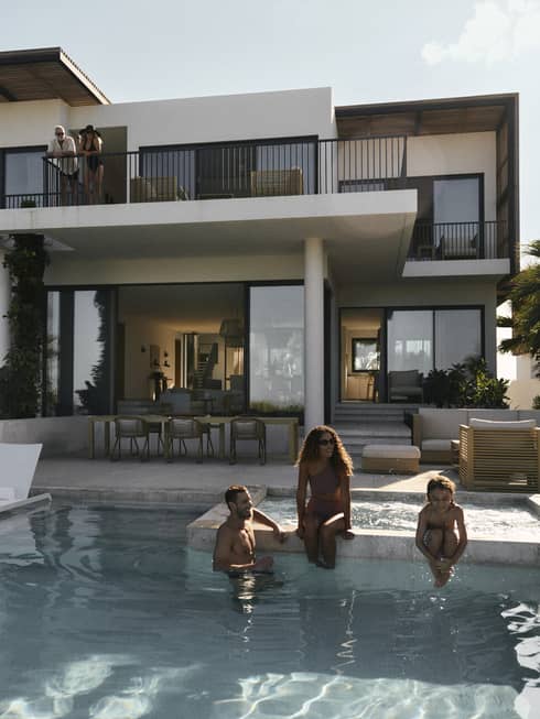 A woman, man and young child sit on edge of private pool at luxury residence in tropical setting