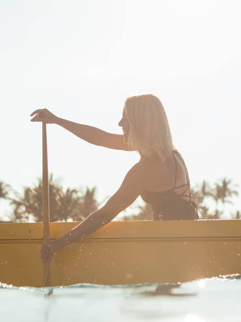 Side view silhouette of woman in swimsuit, man in yellow uniform paddling in yellow canoe, palm trees in background