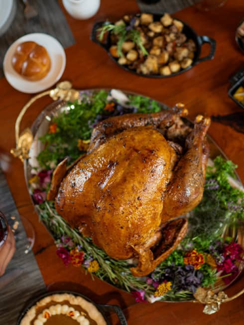 A table with a cooked turkey and Thanksgiving sides around it.