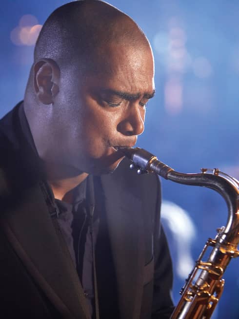 A close up of a man with his eyes closed, playing a saxaphone at a Jazz club in Ten Trinity