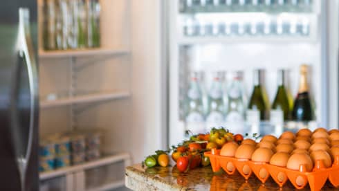 Smiling man holds green bottle in front of open fridge, fresh eggs on counter
