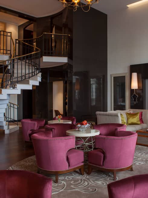 E-Lounge large curved velvet pink chairs around small round tables, modern white spiral staircase in background