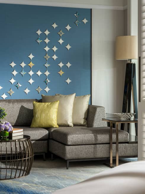 Gold pillows on grey sofa against blue wall with star-shaped Peranakan tile mural