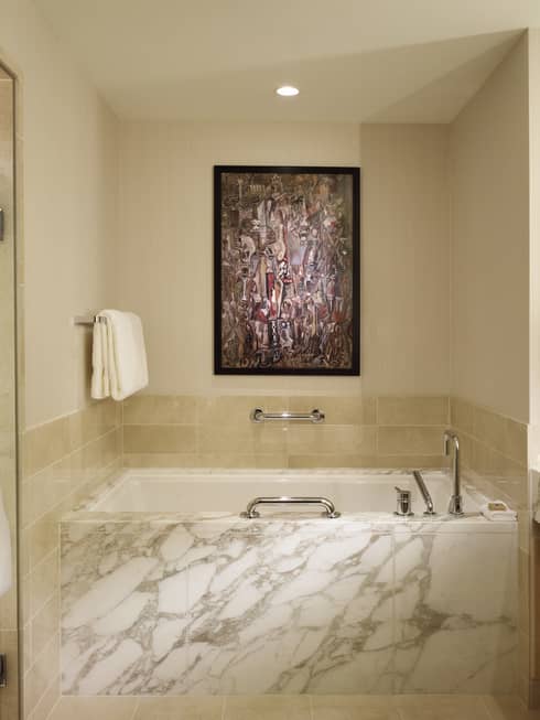 Large white marble bathroom with deep tub in between glass shower, sink and vanity
