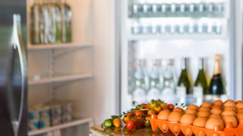 Smiling man holds green bottle in front of open fridge, fresh eggs on counter
