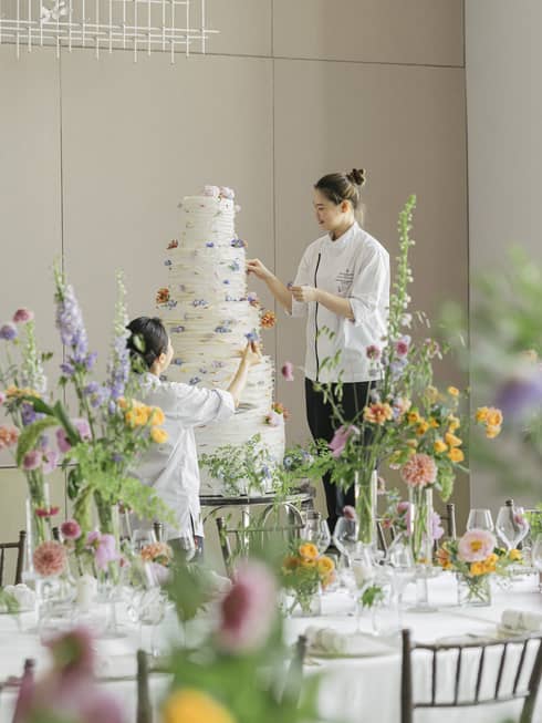 Two chefs decorate a five-tiered wedding cake in ballroom