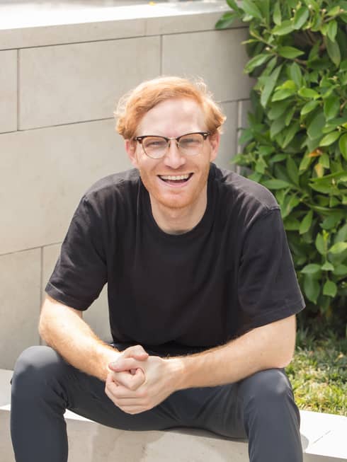 A smiling resident healer Aymeric Vollant sitting on a stone wall