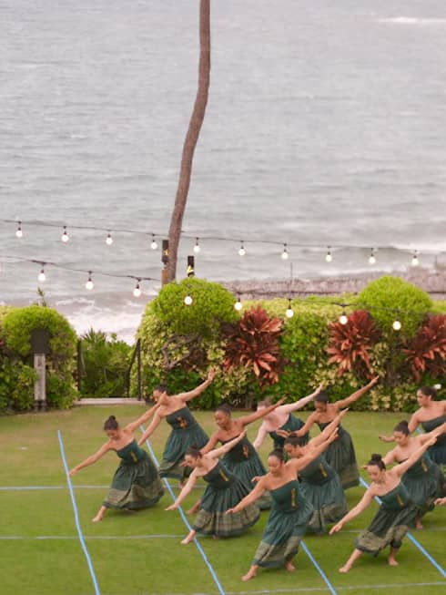 A group of hula dancers perform on an oceanside lawn at luxury resort