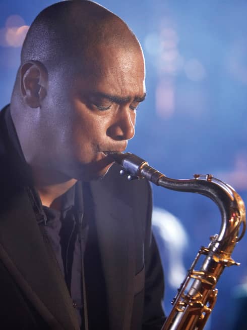 A close up of a man with his eyes closed, playing a saxaphone at a Jazz club in Ten Trinity 