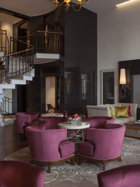 E-Lounge large curved velvet pink chairs around small round tables, modern white spiral staircase in background