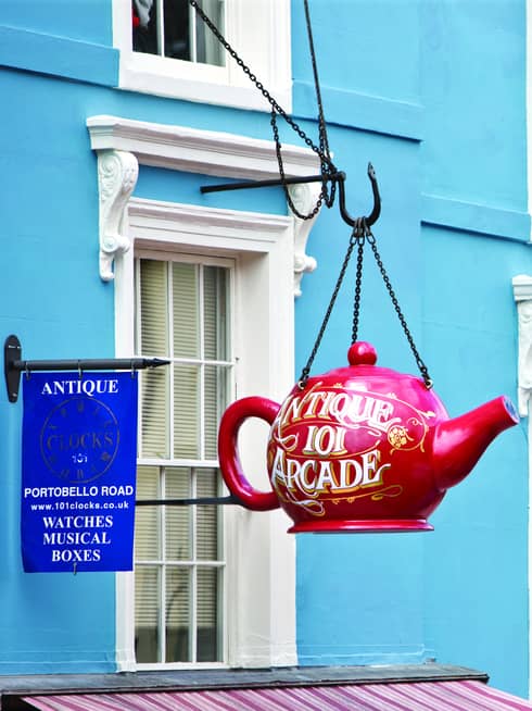 A close up of a red teapot hanging on the exterior of a bright blue building, advertising the Portobello Rd Market