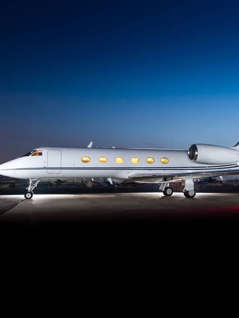 Jet Edge private jet parked on the tarmac at dusk with lights on inside, set against a clear blue sky