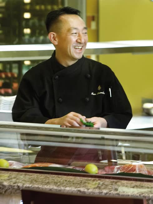 Smiling Chef Masa Shimakawa in uniform at sushi counter
