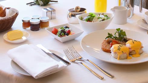 Eggs benedict brunch on plate, fruit and salad in bowls
