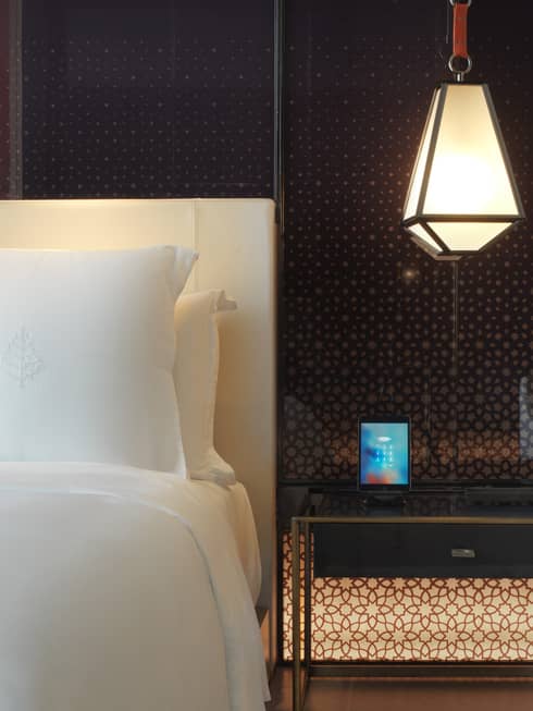 Close-up of modern lantern hanging above nightstand beside white pillow, bed