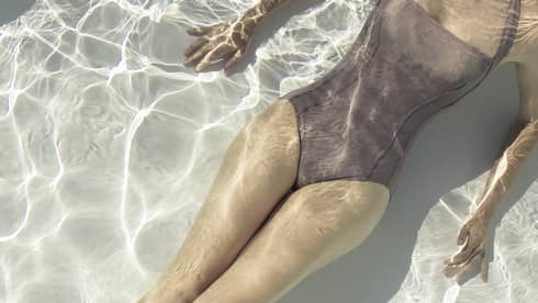 Aerial view of woman in swimsuit's body as she floats under water, sun reflecting in pool