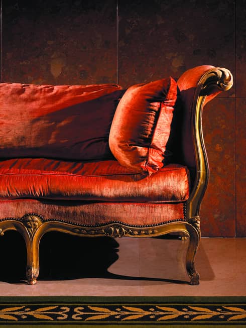 Close up of one end of antique style red velvet sofa in dark room
