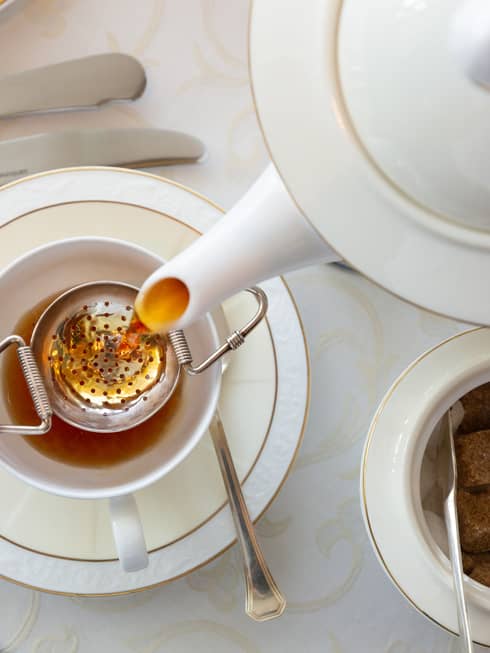 Aerial view of table-setting with a bowl of sugar cubes and mini-tongs, teapot pouring tea over a cup and saucer