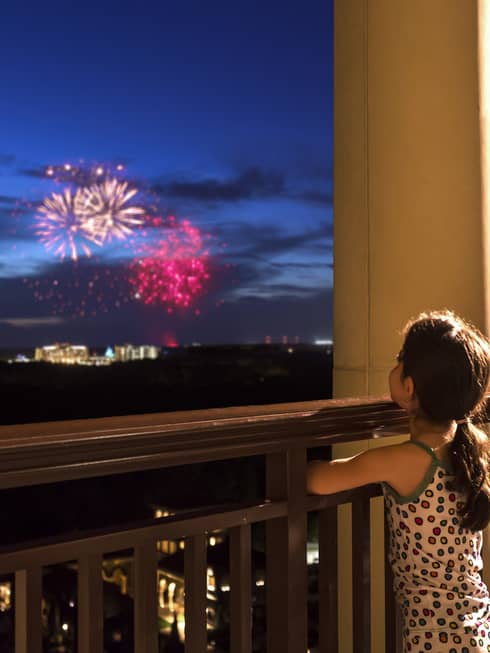 Young girl stands on Four Seasons Hotel balcony, watches colourful fireworks display over Walt Disney World resort