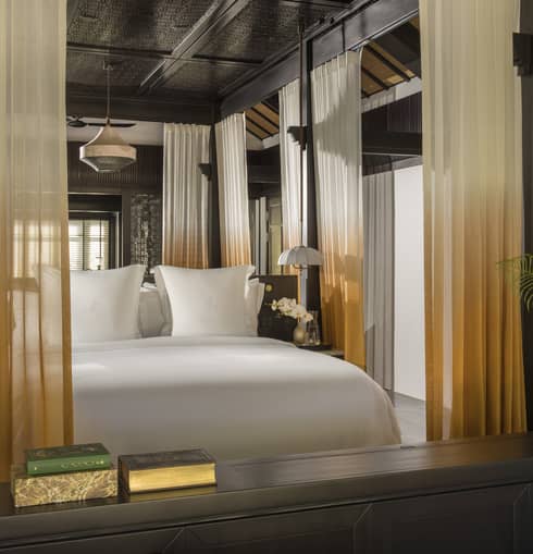 A resort bedroom featuring a king bed with orange and white curtains lining a four-post bed