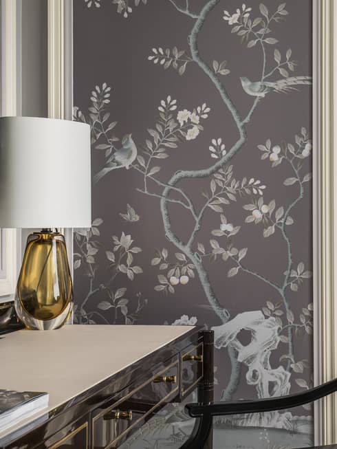 Black desk with orange glass lamp with white shade, wall panel with lilac tone images of trees, birds