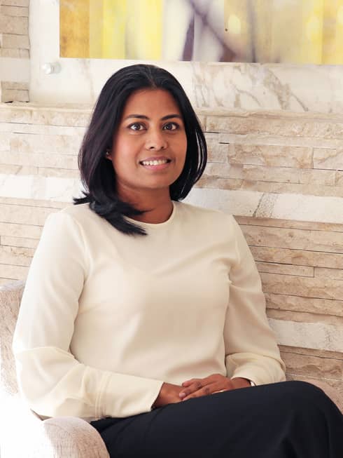 Portrait photo of Tania Bardhan sitting in chair against wood wall
