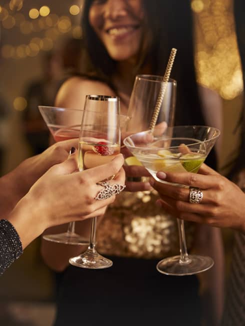 Four women in evening wear clink their cocktail glasses