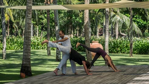 Yogi helps two people with yoga poses on wood platform under canopies
