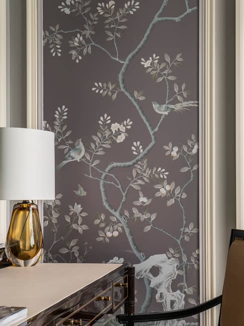 Black desk with orange glass lamp with white shade, wall panel with lilac tone images of trees, birds