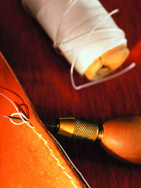 A close up of sunlight illuminating a piece of leather that has thread looped through it, as it is in process