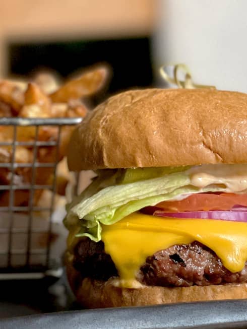 A burger with lettuce, tomato and cheese next to a small basket of fries.