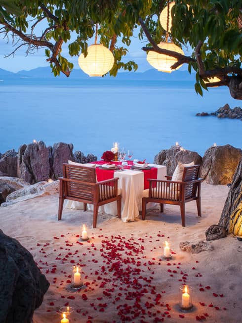 A table set for dining overlooking the pale blue waters with soft lantern and candle-lit glow