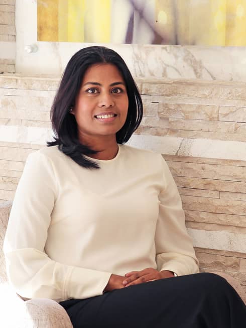 Portrait photo of Tania Bardhan sitting in chair against wood wall