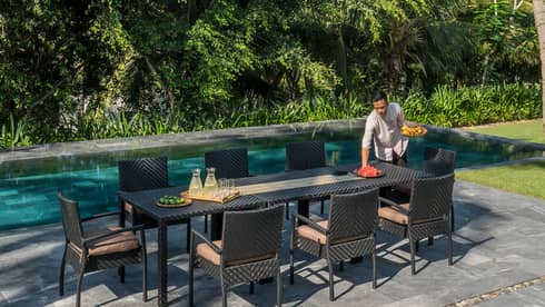Server sets long patio dining table by Hilltop Villa outdoor swimming pool