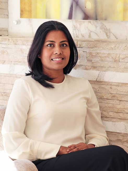 Portrait photo of Tania Bardhan sitting in chair against wood wall
