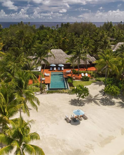 Aerial view of Bora Bora villa with pool on edge of beach, surrounded by palm trees