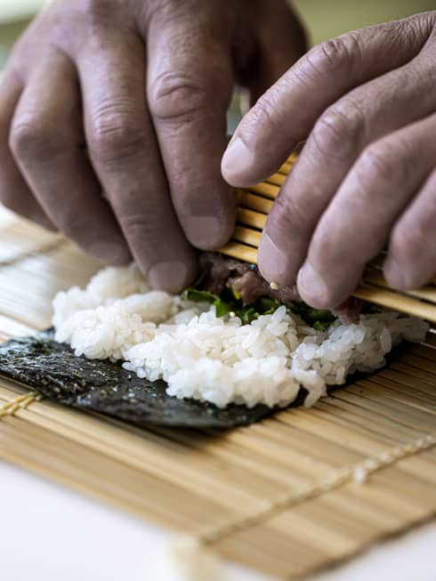 A four seasons chef rolls sushi with a bamboo mat