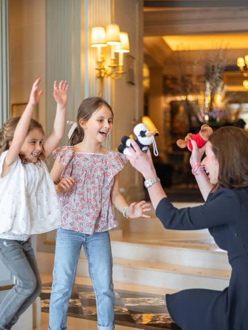 Concierge crouched, holding two stuffed animals toward excited, smiling girls