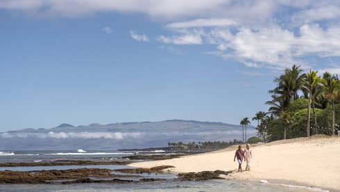 A couple walks along the beach in Hualalai near Four Seasons Resort Hualalai
